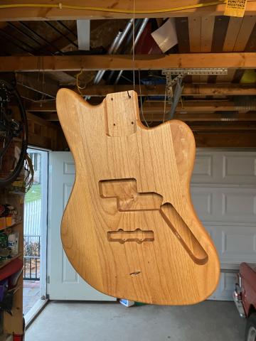 the bare bass body hanging from a wire after a coat of varnish