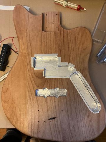 bass guitar body showing aluminum tape lining the cavities in the body that will hold the pickups and wiring