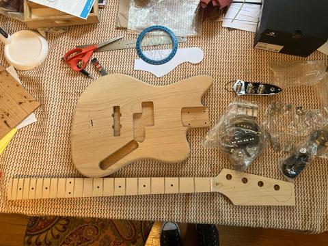 the pieces of a bass guitar kit arranged on a wooden table