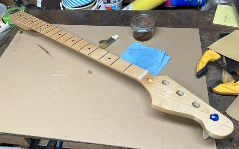 finishing the bass neck, showing a jar of varnish and brush with neck propped up on pegs