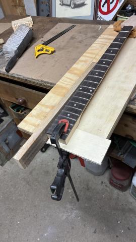 bass neck on a plywood board, with long sanding block along the left side