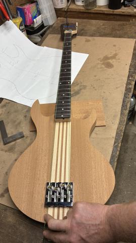guitar body and neck, lined up as if assembled, with pieces of string held in place of the guitar strings