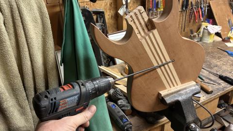 Guitar body held in a vise with a long drill bit going in at a very oblique angle
