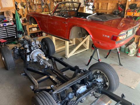 car chassis on the floor with engine and wheels, next to a body tub on a wooden platform