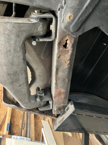 view from below a car, showing rust holes in the frame