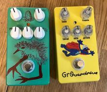 two painted and assembled pedals, one is a grassy green with a black drawing of a baby bird, the other yellow with a painting of super grover